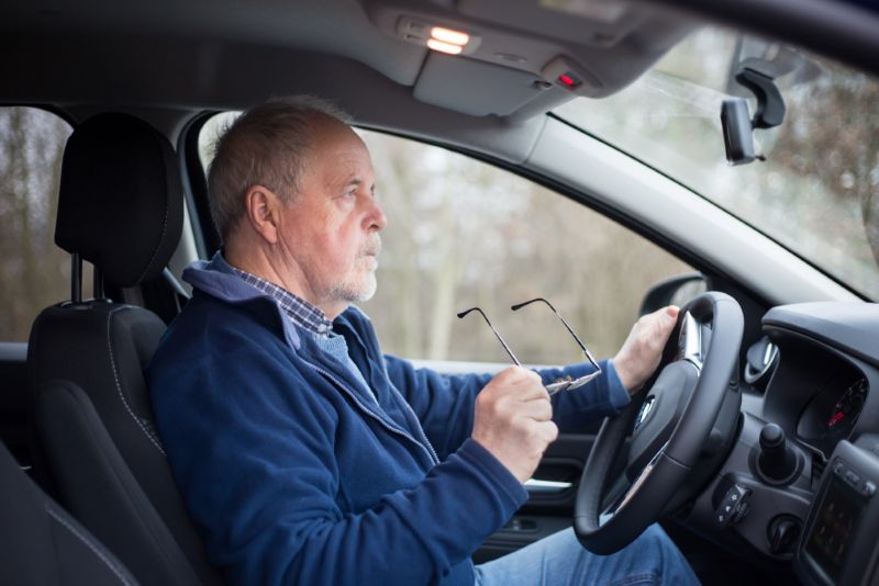 older man holding glasses while driving