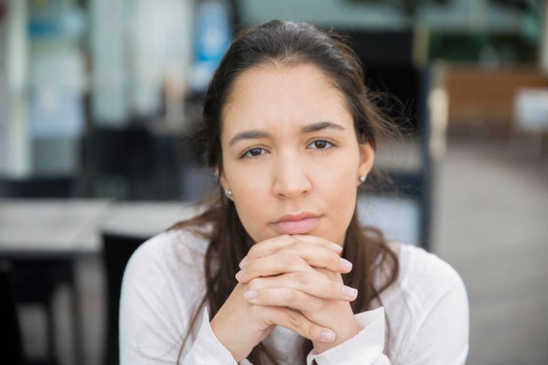 Young woman sitting with hands clasped looking into camera